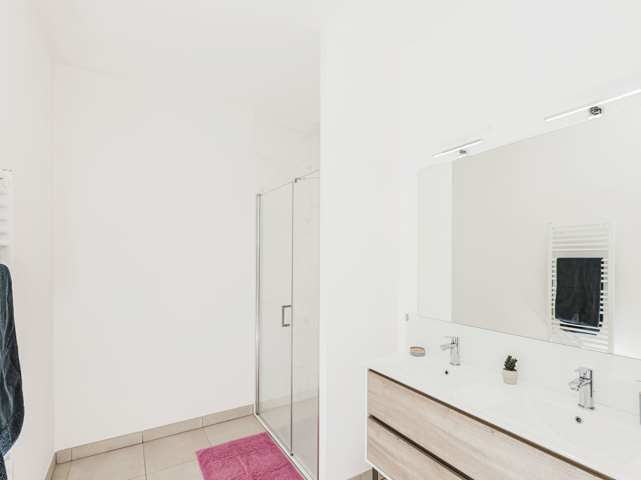 A modern bathroom with a glass shower enclosure, a white sink with a mirror, and a wooden vanity.