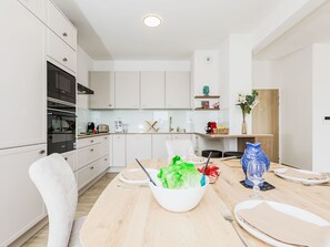 A modern kitchen with white cabinets, a dining table set for two, and a variety of kitchen appliances. - Newquay by Interhome (Dinard)