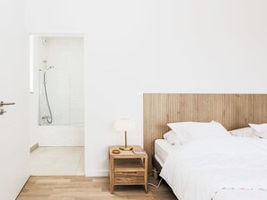 A bedroom with a wooden headboard, a bedside table with a lamp, and a shower area. - Newquay by Interhome (Dinard)