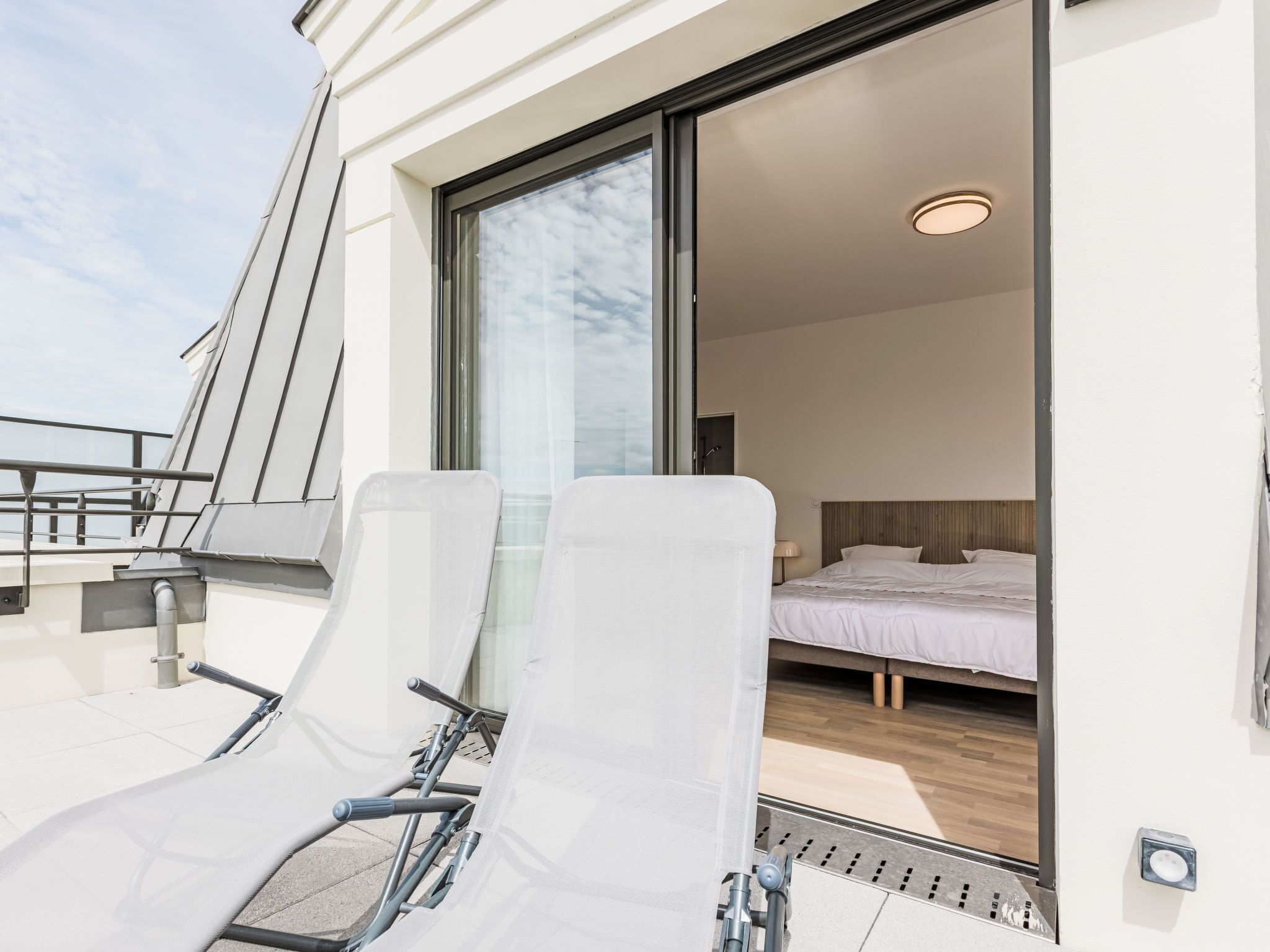 Una habitación de hotel moderna con un amplio ventanal corredero que da a un balcón con dos sillones blancos.