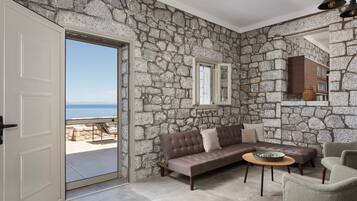 A room with a stone wall, a sofa, a round table, and a view of the sea through a door.