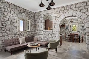 A room with stone walls, a sofa, chairs, a table, and a dining area.
