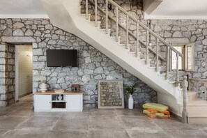 Eine Steinsäule, eine Treppe, ein Flachbildfernseher, ein weißes Schränkchen und ein gerahmtes Bild.