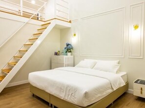 A bedroom with a bed, a white nightstand, a dresser, a white wall with a light switch, and a staircase. - British Hill Resort (Sattahip)