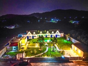 A large, multi-story hotel with a well-lit lawn and a swimming pool.