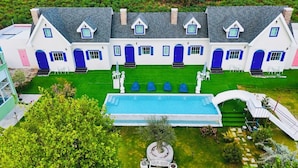 Una casa grande y moderna con piscina, varias puertas azules y un césped cuidado.
