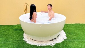 Una bañera grande con grifo dorado, rodeada de guijarros blancos y césped artificial verde.