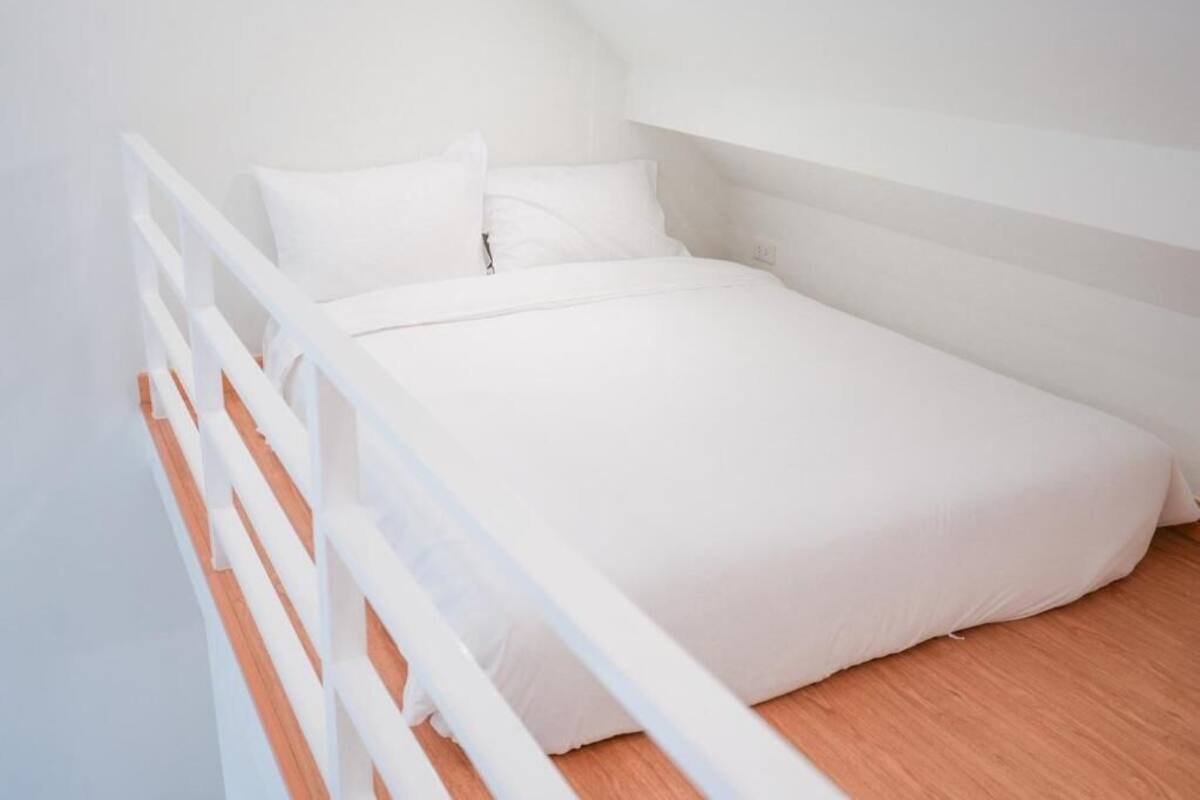 Una cama blanca en una habitación con techo inclinado y suelo de madera.
