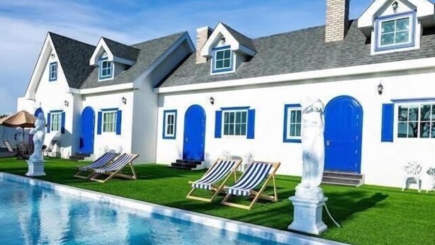 Una casa grande con piscina, varias puertas azules y una estatua.