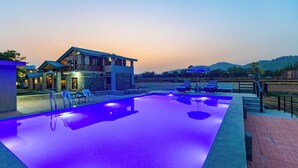 Una piscina con bordo illuminato di blu, sedie a sdraio e un edificio con un balcone.