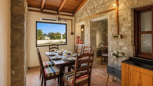 Zona pranzo con parete in pietra, soffitto in legno e vista dalla finestra.