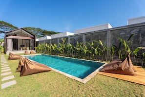 Uma piscina com água azul cristalina, rodeada por um gramado e um muro de concreto.