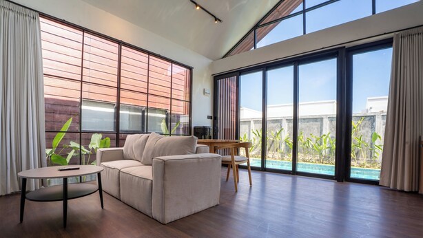 A modern living room with a sofa, a round table, and a view of a swimming pool.