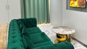 A modern living room with a green sofa, a round gold table, and a TV mounted on the wall.