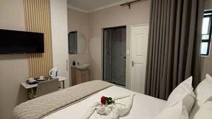 A hotel room with a bed, a TV, a desk with a kettle, a mirror, and a door.