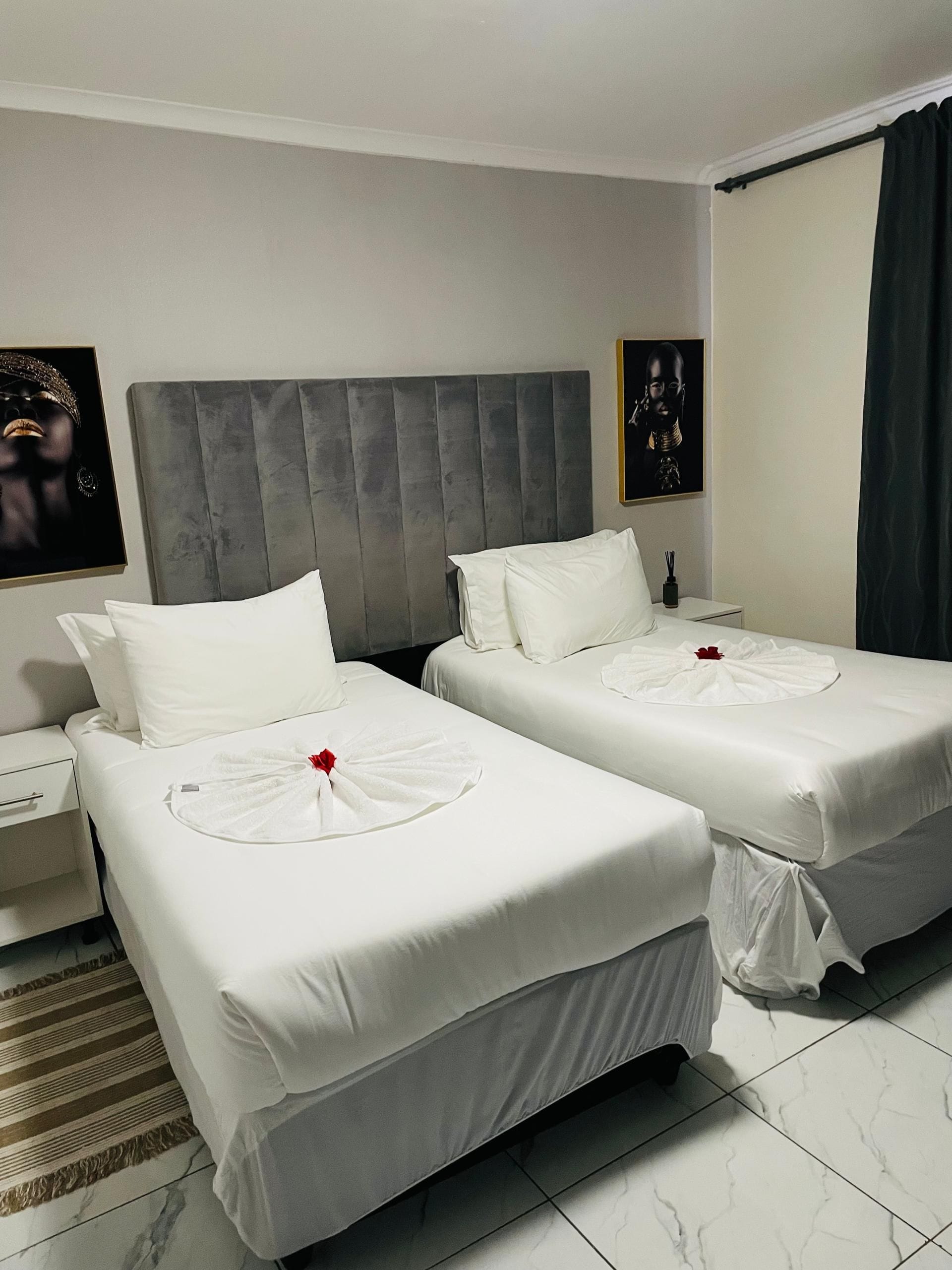 A hotel room with two beds, a grey headboard, white bedding, a striped rug, and artwork on the walls.