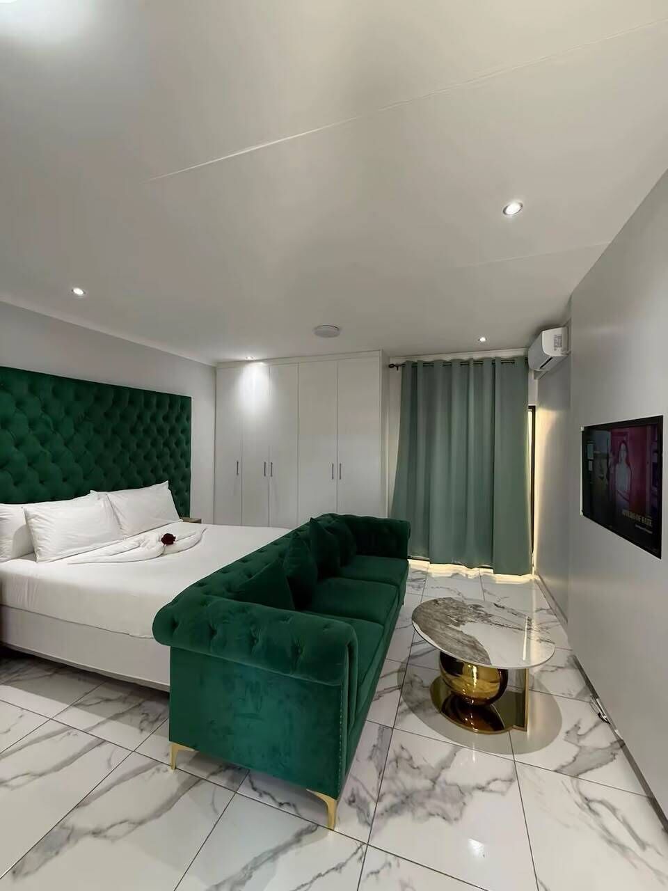 Un dormitorio moderno con cama, sofá verde y suelo de mármol.