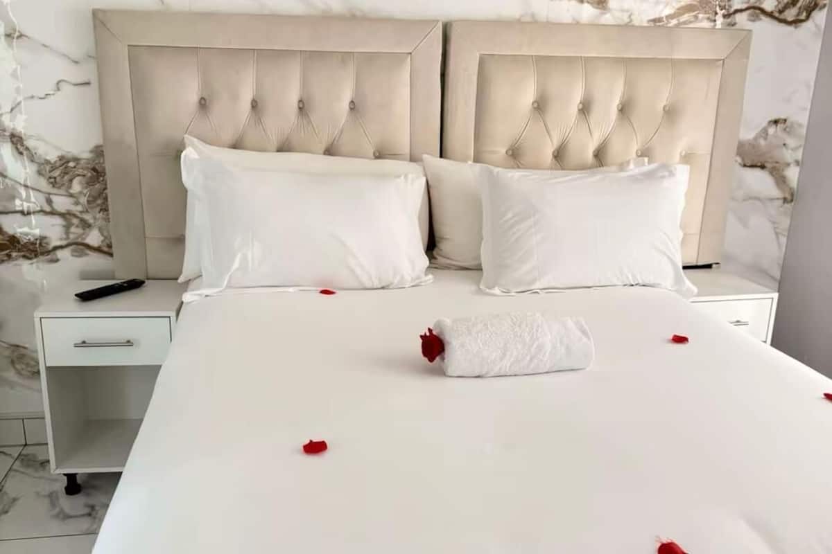 A hotel room with a large bed, two nightstands, a marble-patterned wall, and a white bedspread with rose petals.