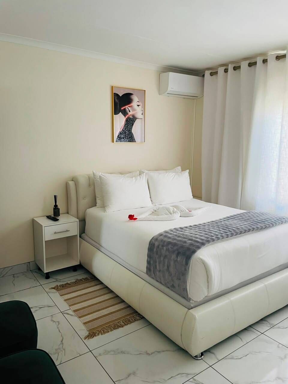 A hotel room with a bed, a nightstand, a wall-mounted air conditioner, and a window with curtains.