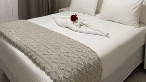 A neatly made bed with a white comforter, a fluffy blanket, and a red rose.
