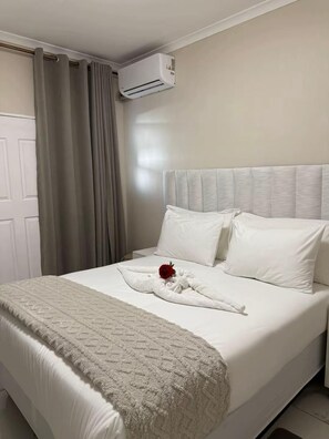 A neatly made bed with a white comforter, a fluffy blanket, and a red rose.