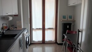 Cozinha compacta com máquina de lavar, pia e área de refeições com uma cadeira.