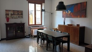 Uma área de refeições com mesa, cadeiras, luminária, armário e janela com persianas.
