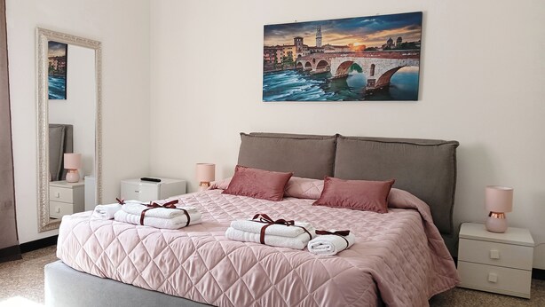 Quarto com cama, almofadas, mesa de cabeceira, espelho e um quadro pendurado na parede.