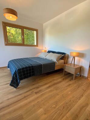 A bedroom with a bed, bedside table, lamp, window, and wooden flooring. - MAISON OLIVIER (Veigy-Foncenex)