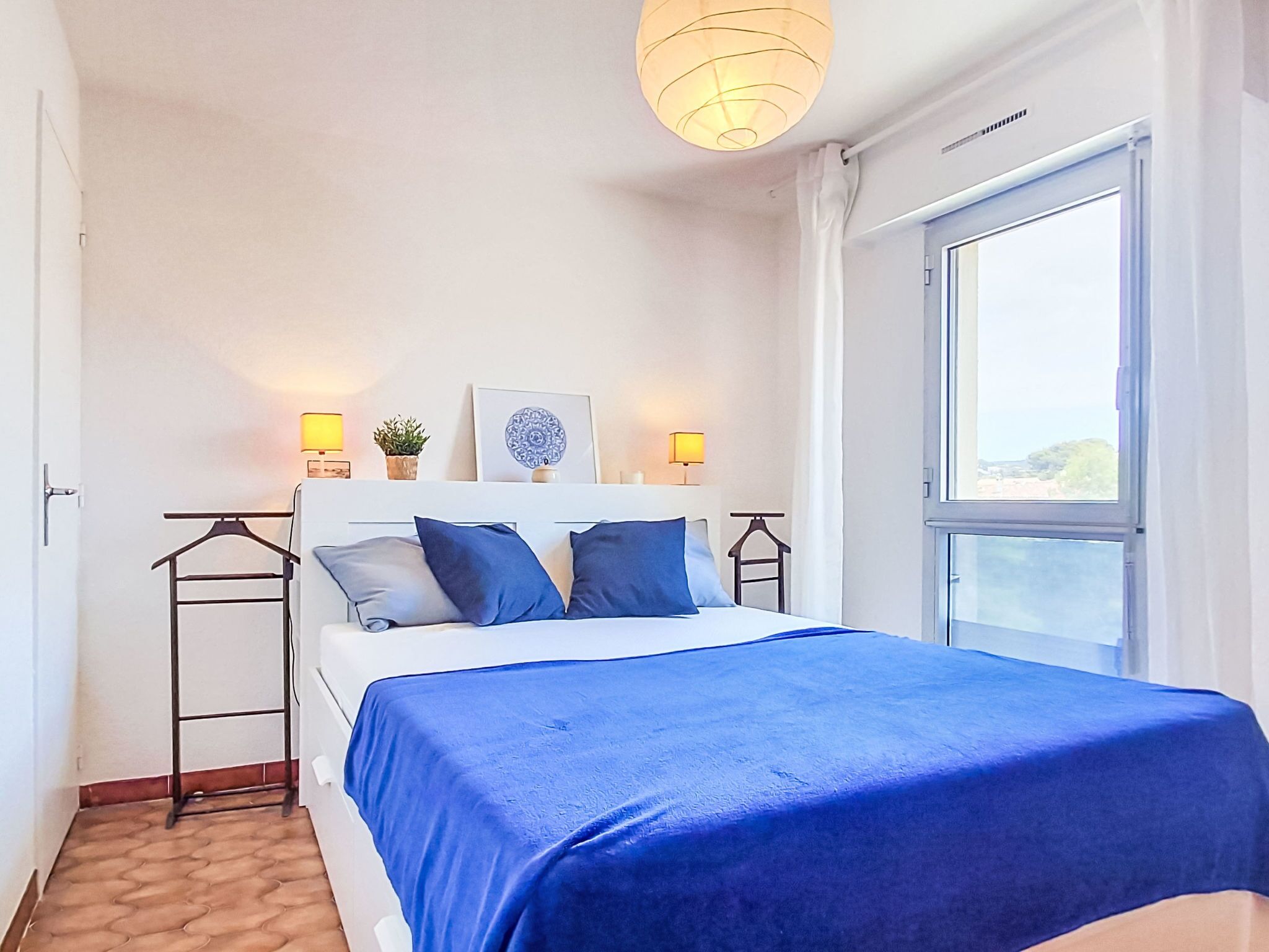 Een slaapkamer met een bed, nachtkastjes, een hangplant en een raam.