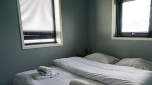 Ett rum med två sängar, båda med vita lakan och kuddar, och två fönster med persienner.