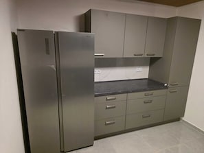 Eine Küche mit einem Edelstahl-Kühlschrank, grauen Schränken und einer Marmor-Spritzschutzwand.