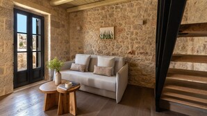 A stone-walled room with a sofa, a small wooden table, and a staircase.