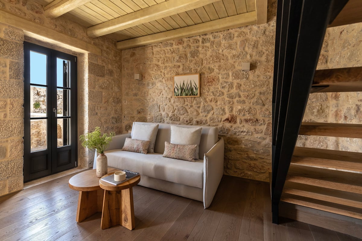 Una habitación con paredes de piedra, un sofá, una pequeña mesa de madera y una escalera.