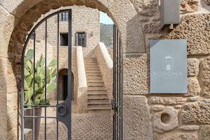 A stone building with a sign for 'Korona Boutique Hotel' and a cactus plant visible through a metal gate. - Korona Boutique Hotel  (Itilo)