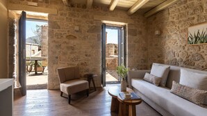 A stone-walled room with a sofa, a chair, a small table, and a door leading outside.