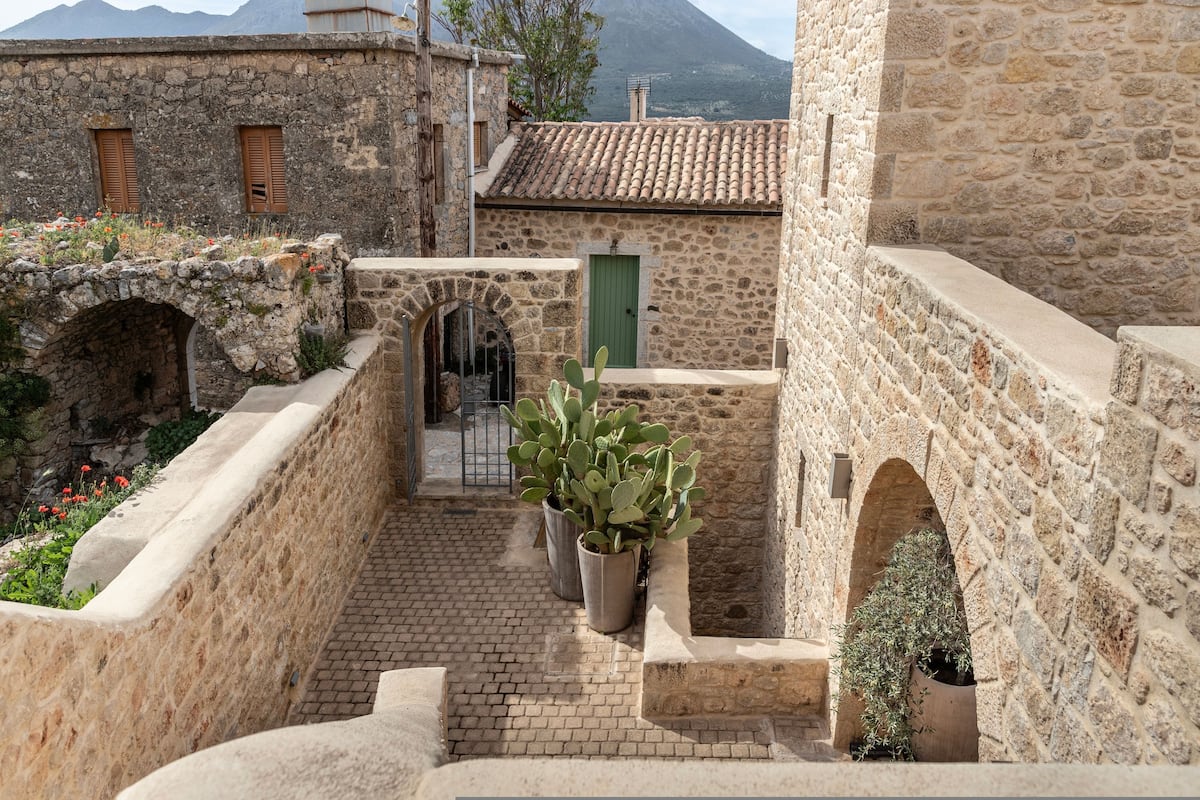 Un patio de piedra con una puerta verde, cactus en macetas y un muro de piedra.