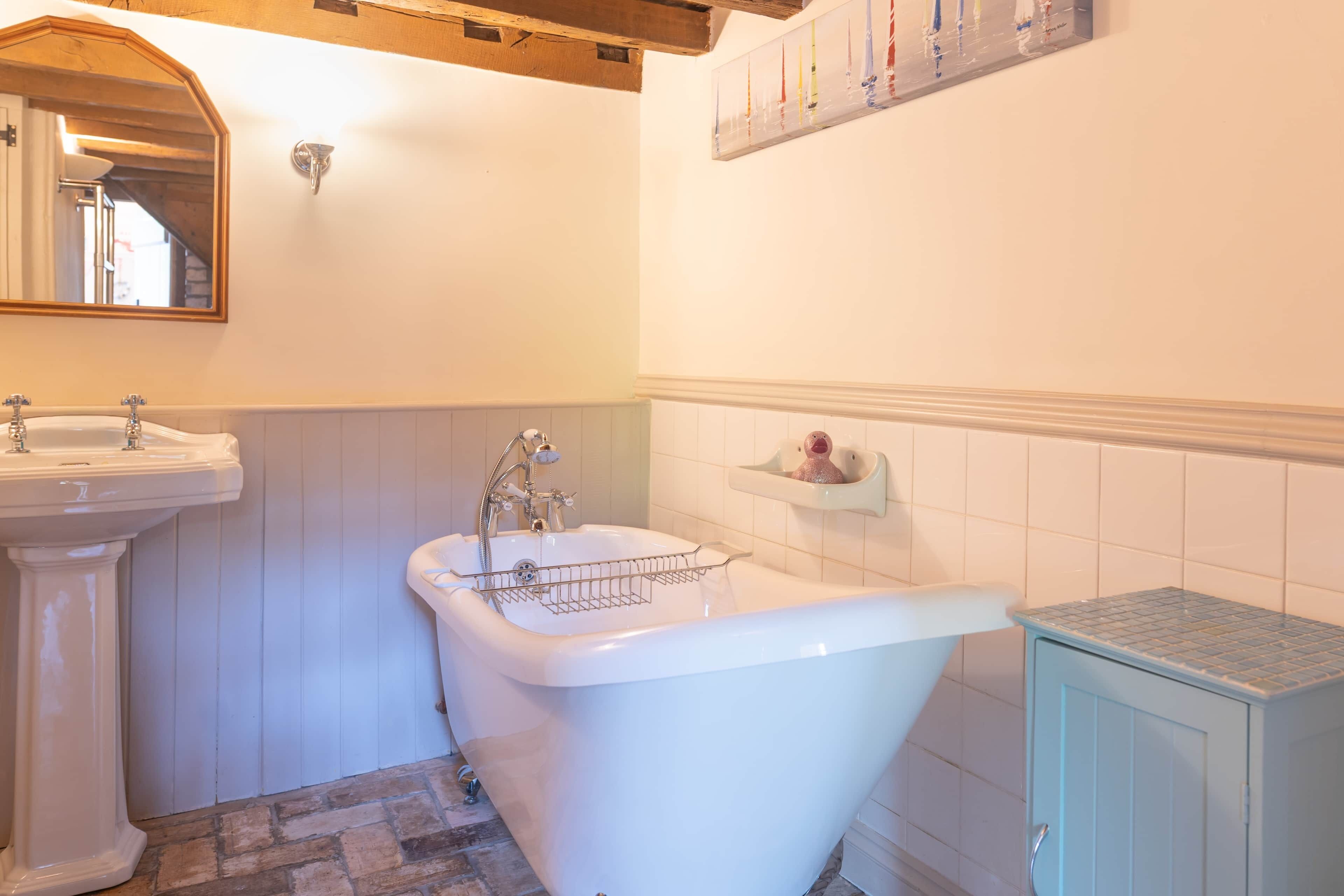 Une salle de bain avec une baignoire sur pieds, un lavabo sur colonne et un meuble de rangement.