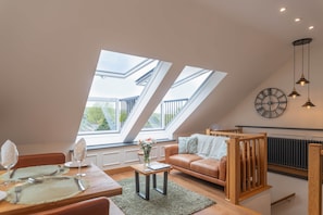 Ein modernes Loft mit Dachfenstern, einem Essbereich, einer Couch und einer Wanduhr.