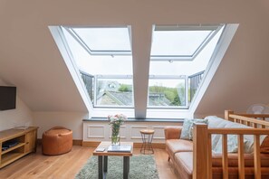 Ein Schlafzimmer im Loft-Stil mit Dachfenstern, einem Holztisch, einer Couch und Blick auf die Nachbarschaft.