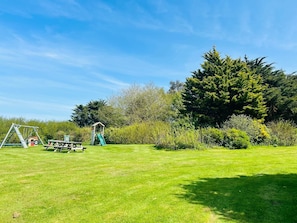 A grassy outdoor area with a swing set, a small playhouse, and a large tree.