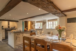 A kitchen with a central island, wooden dining table set for six, and a stone wall.