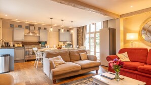 A modern kitchen with white cabinets, a dining area with a beige sofa, and a red sofa in the living room. - Dollys Barn - Ilfracombe (Near Woolacombe) (Ilfracombe)