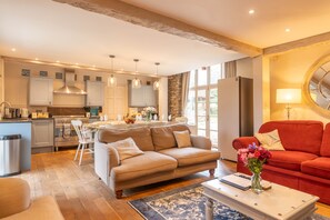 A modern kitchen with white cabinets, a dining area with a beige sofa, and a red sofa in the living room. - Dollys Barn - Ilfracombe (Near Woolacombe) (Ilfracombe)