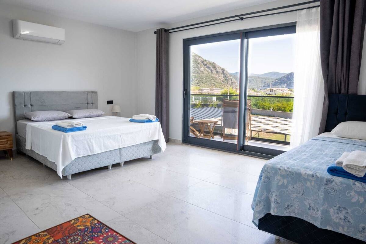Ein Hotelzimmer mit einem Bett, einem zusätzlichen Bett, einer großen Schiebeglasdoor zum Balkon sowie einem kleinen Tisch mit Stühlen.