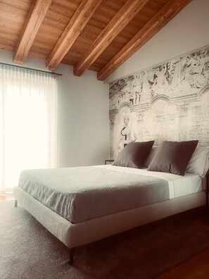 A bedroom with a bed, wooden ceiling beams, a mural on the wall, and a window with curtains. - Agriturismo Camerin - CL Agri Lounge (Conegliano)