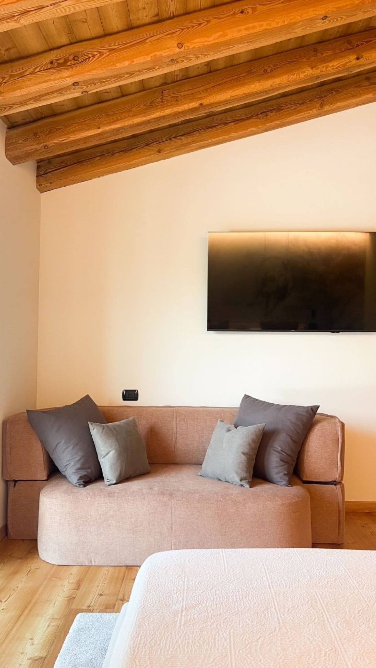 A modern living room with a wooden ceiling, a sofa with cushions, and a flat-screen TV mounted on the wall.