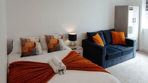 A hotel room with a bed, a blue sofa, and a nightstand with a lamp. - The Snug by JS Apartments (Blackburn)