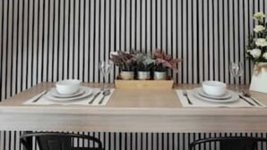 A dining table set with plates, bowls, and cutlery, flanked by chairs, against a striped wall. - The Snug by JS Apartments (Blackburn)