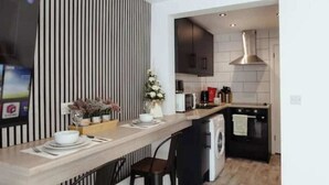 A modern kitchen with a central island, a washing machine, and a dining area with chairs. - The Snug by JS Apartments (Blackburn)